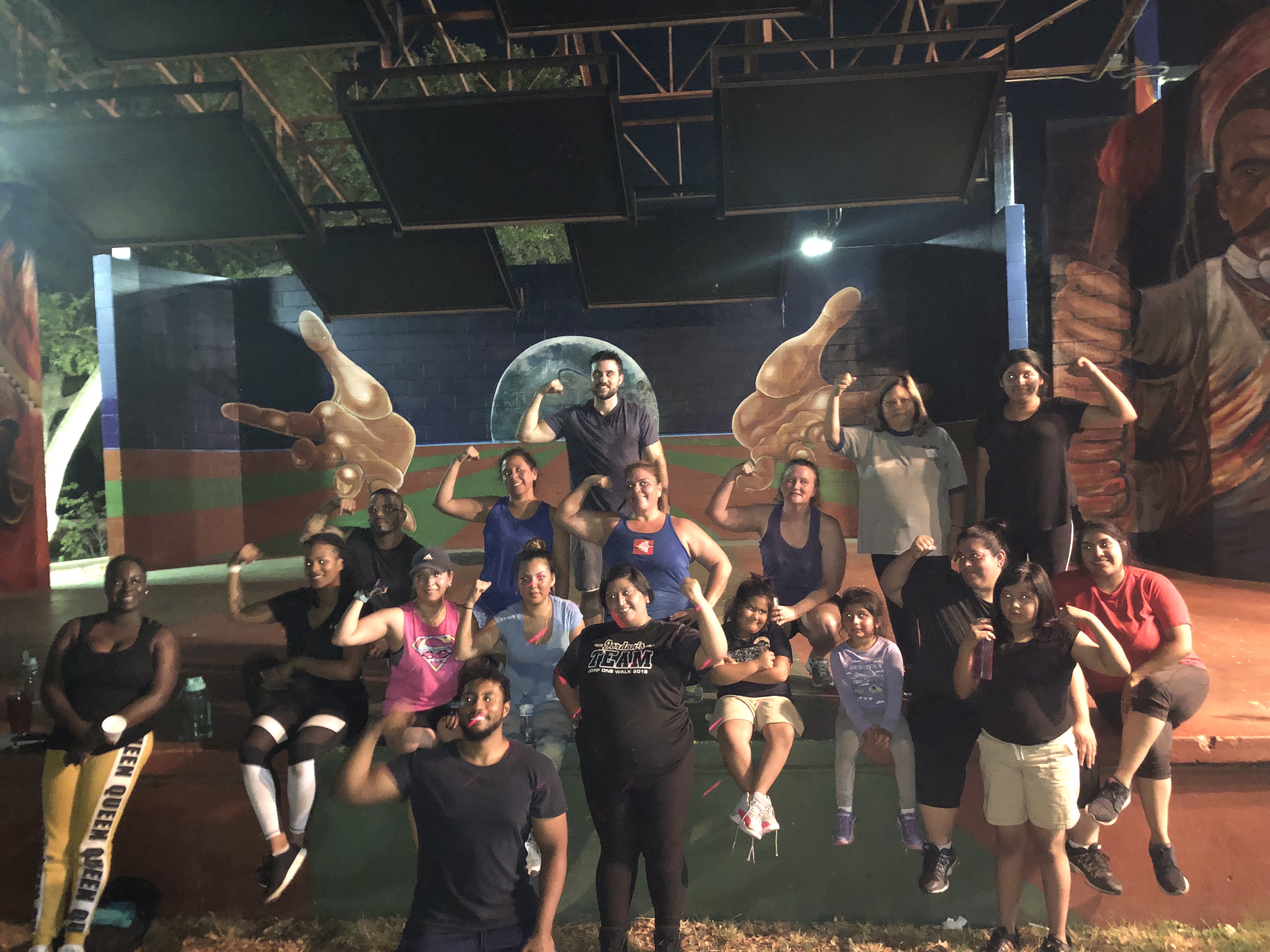 A group of men and women in workout gear pose in front of a mural after having participated in an east Austin Boot Camp class.